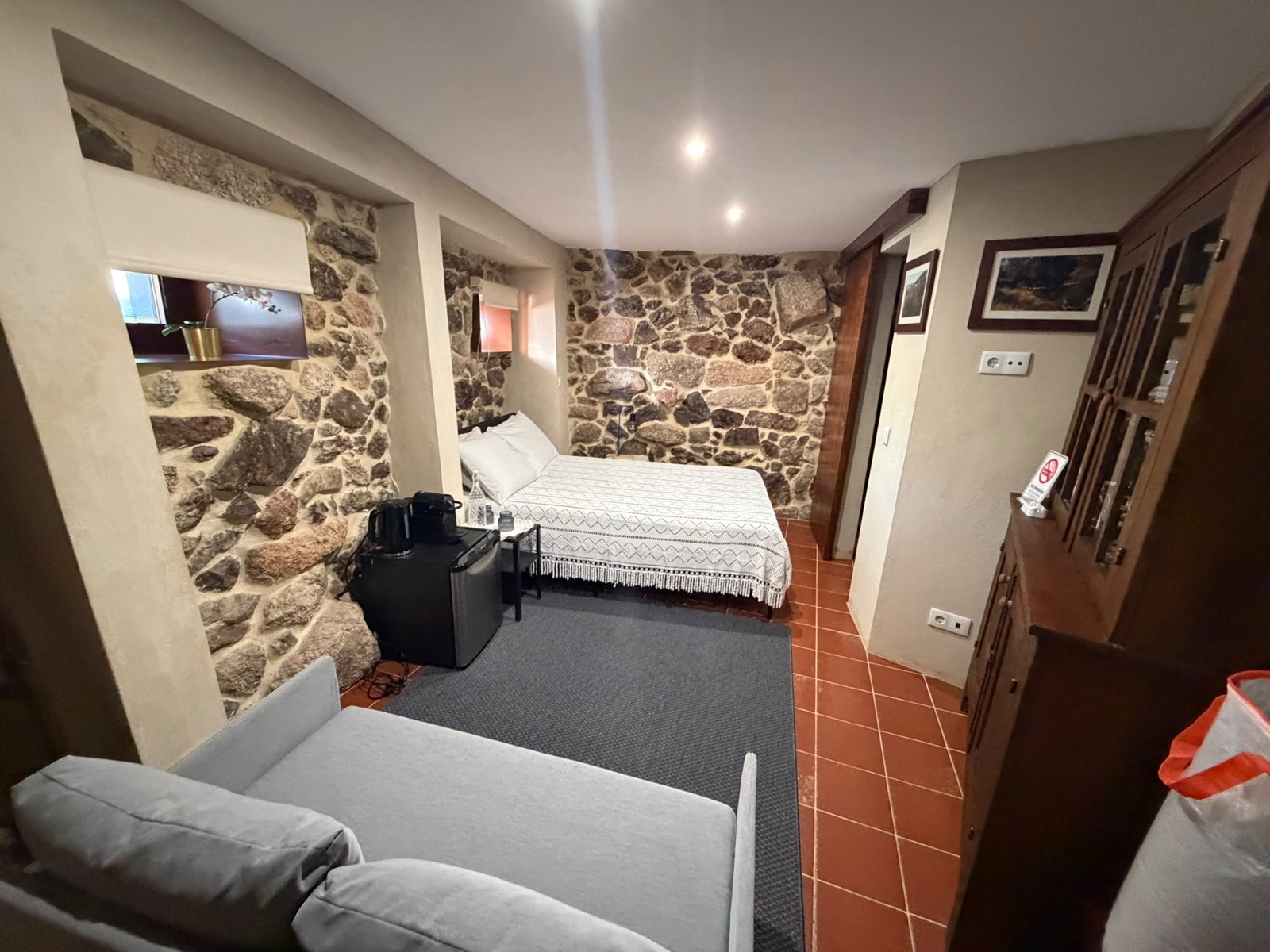 Quarto do T0, com cama de casal e paredes em pedra
